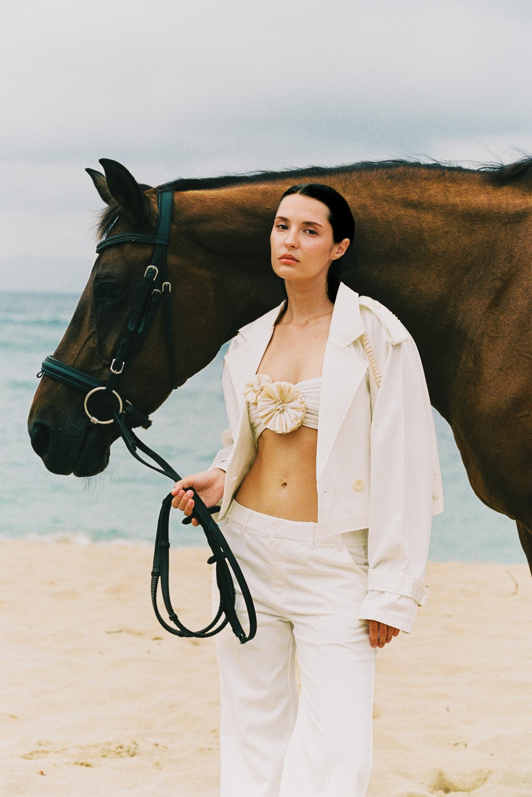 Femme en veste et pantalon blancs tenant un cheval sur la plage, Poupette St Barth