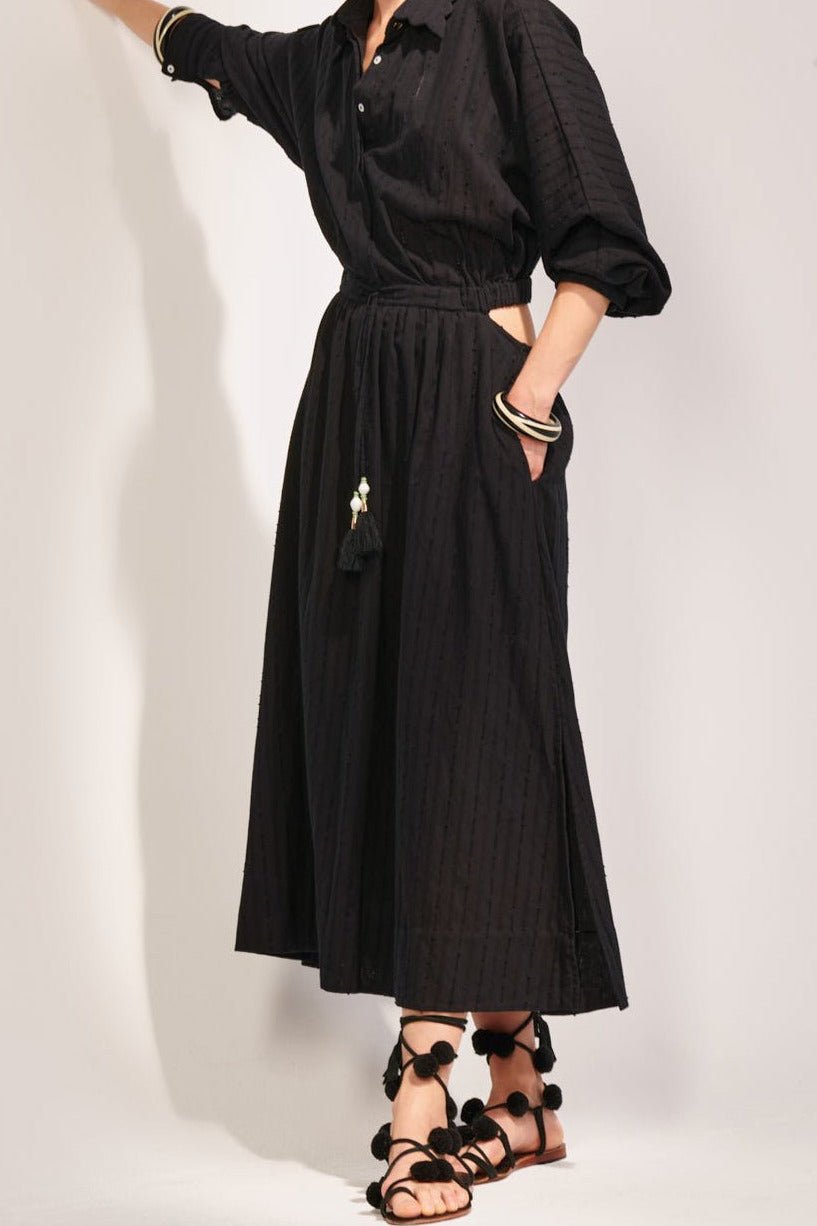 Black long dress – Long Dress Sunniva by Poupette St Barth, posed against a wall with side cutout